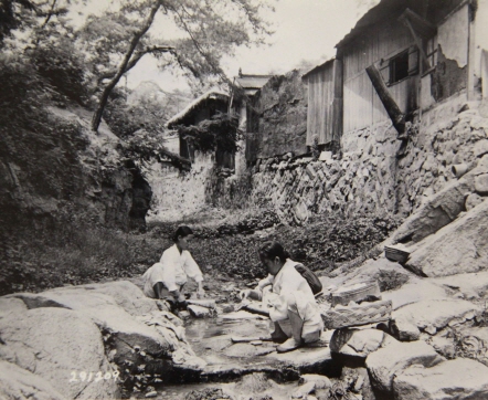 한국인 주부 2명이 집 근처 개울에서 가족들의 빨래를 하고 있다. 사진을 찍은 미국병사는 ‘비누가 부족하고 한국 전통의 흰 옷을 빨기 힘든 조건에도 불구하고 이들은 자신들의 원칙을 고수하고 있다.’고 평하고 있다. 평생 한 일이기 때문에 편하게 쪼그려 앉아 나무방망이로 빨래를 두드리고 있다.(1947) 